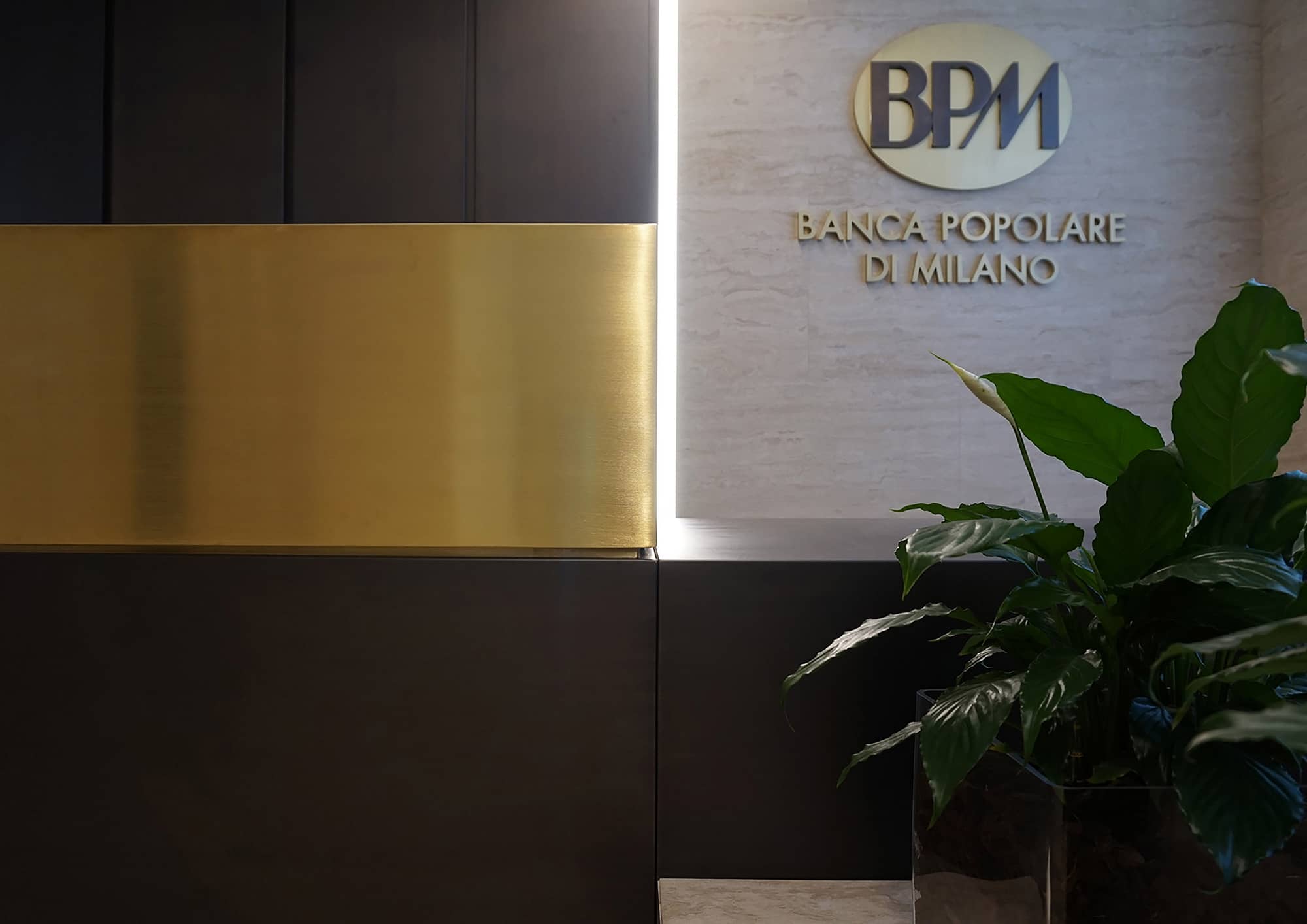 Banco BPM Foyer, vista di dettaglio su desktop reception in noce e ottone e marchio su parete di fondo