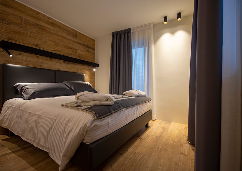 Hotel Rascard, vista angolare su camera letto con testata rivestita in ceramica effetto legno