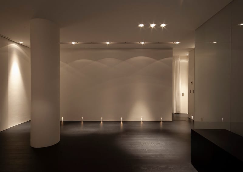 Attico CC, parete bianca con faretti incassati a parete e a soffitto, pavimento parquet scuro